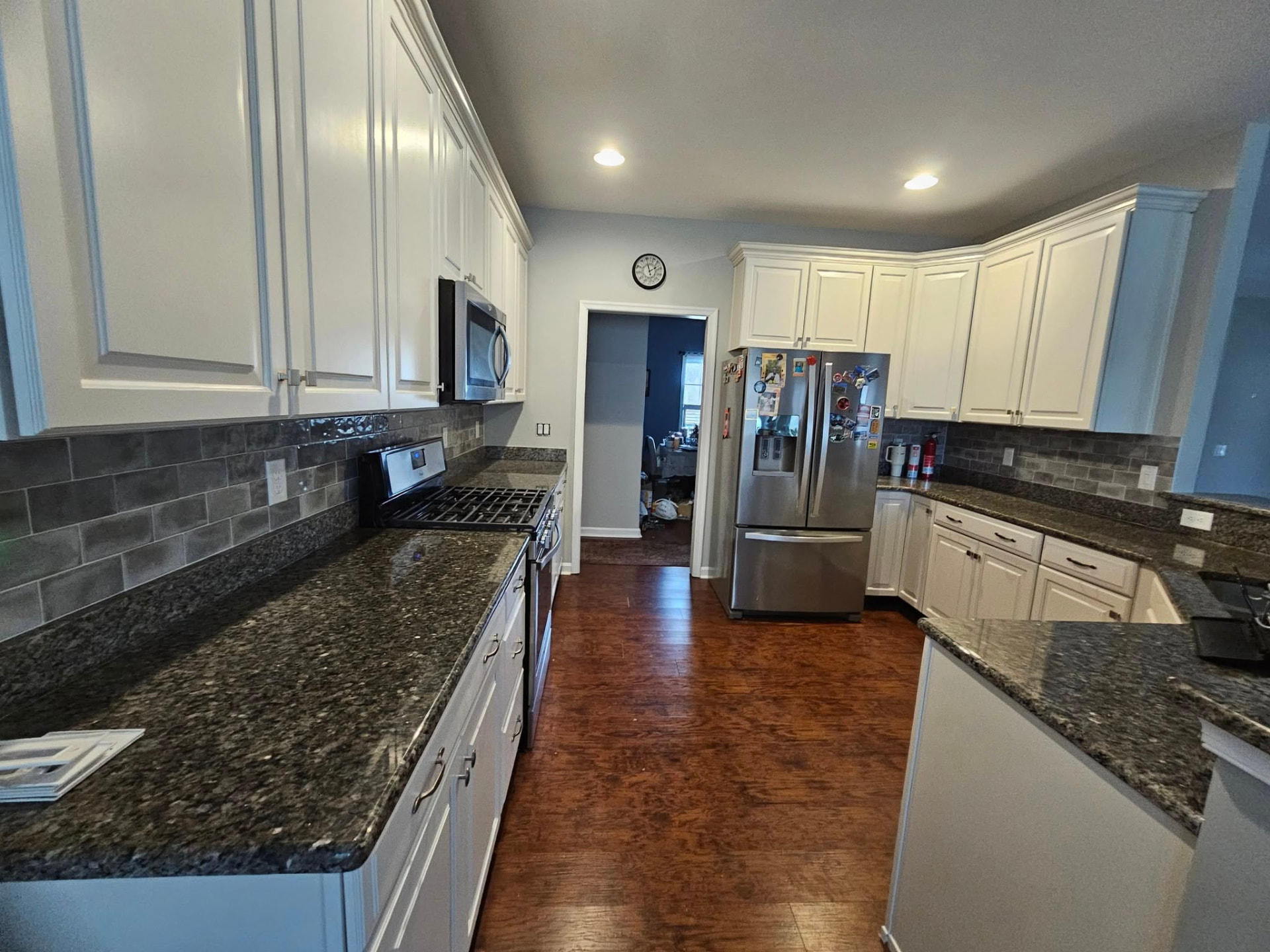 Galley kitchen with cabinets refinished in warm white against dark granite and a grey tile backsplash