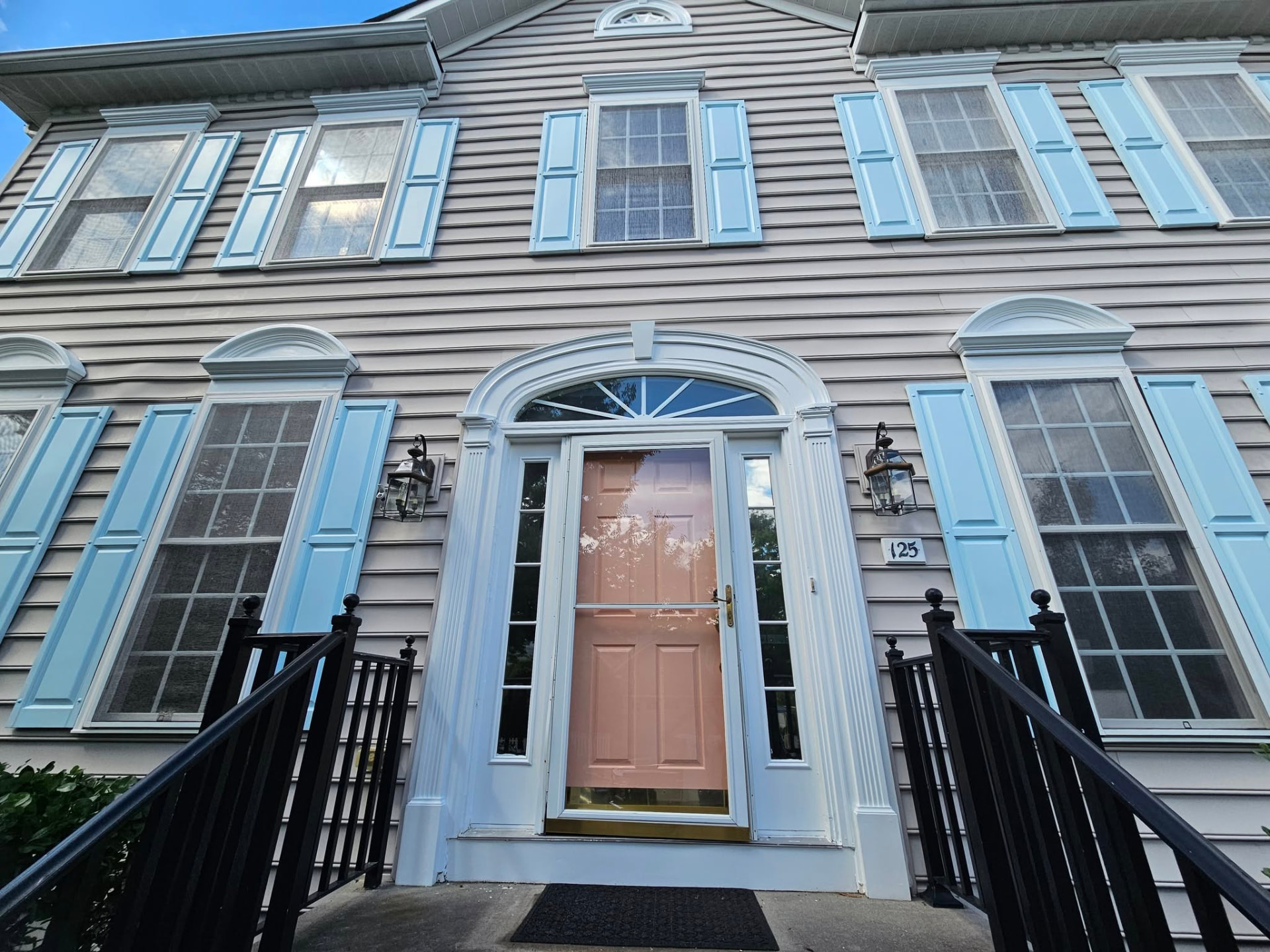 Same colonial with soft blue shutters, a blush front door, and crisp white trim