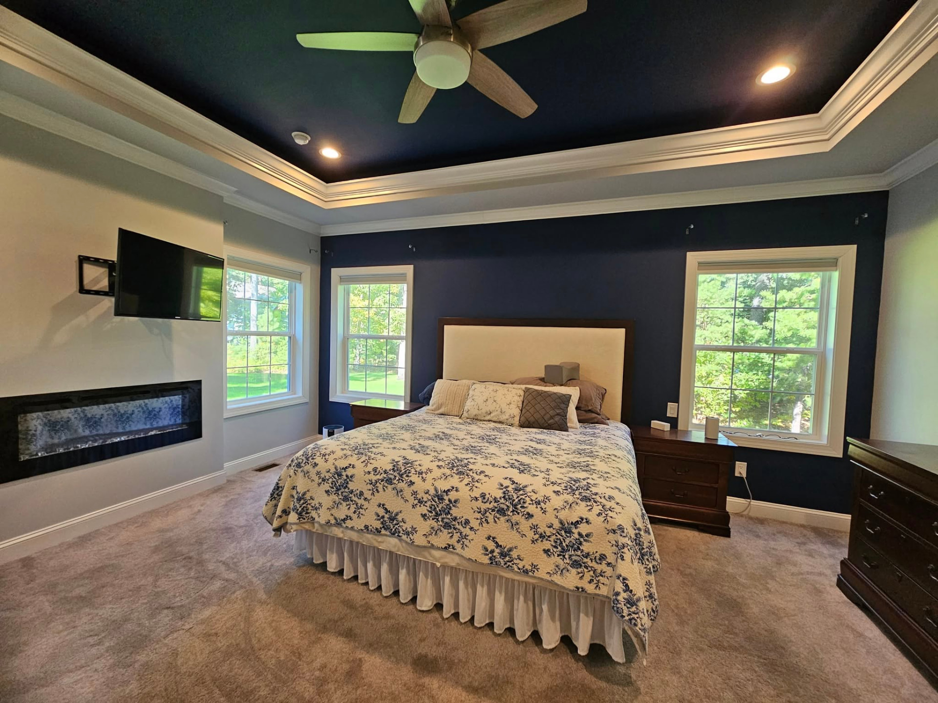 Primary bedroom with navy walls and a matching navy tray ceiling framed by white crown moulding