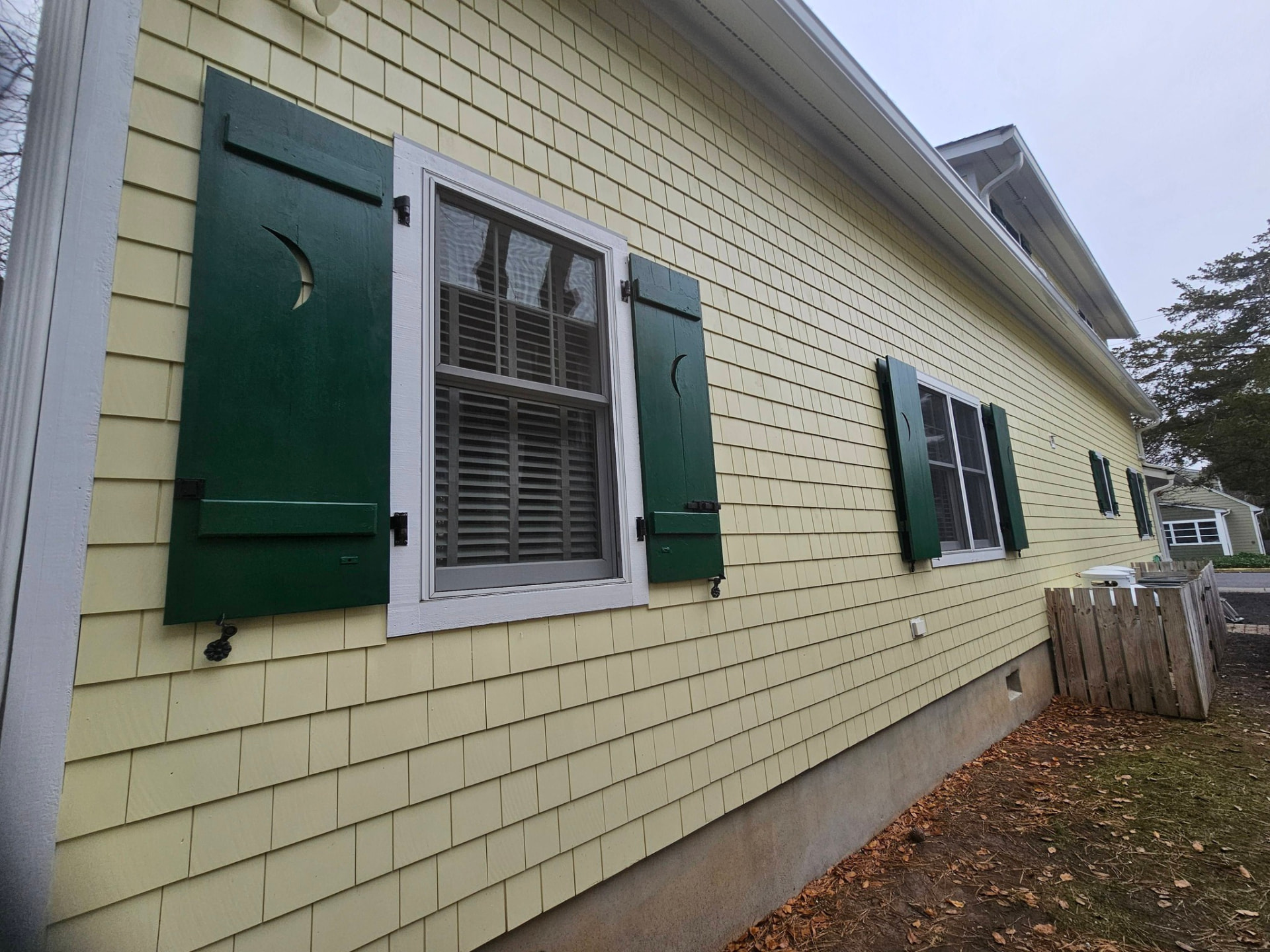 Same shutters repainted a deep forest green with crisp white window casings and refreshed butter-yellow siding