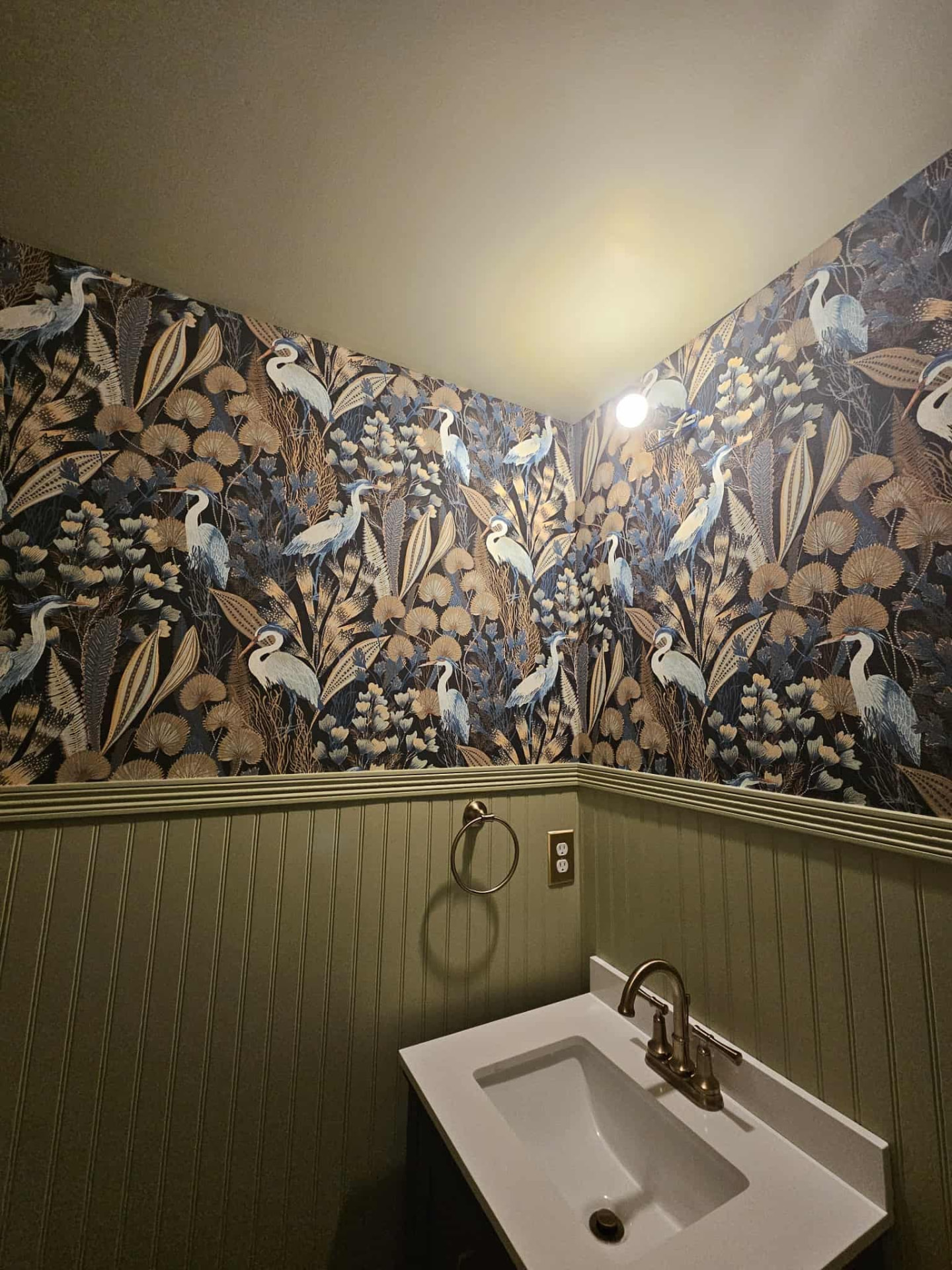 Powder room with navy heron and botanical wallpaper above sage green beadboard wainscot