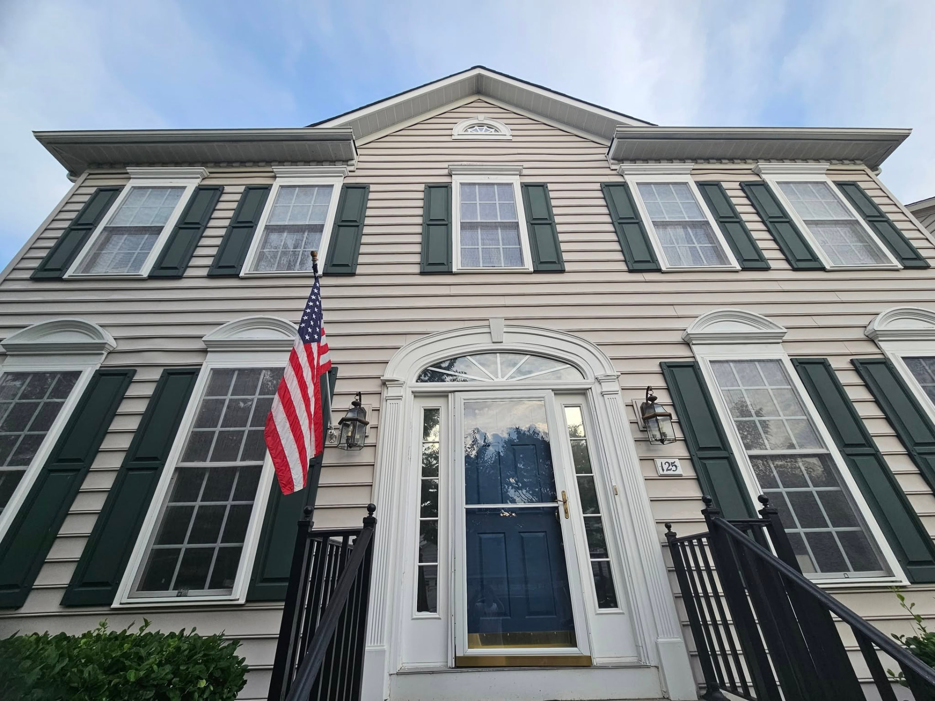 Colonial home with beige siding, dark green shutters, and a navy front door before painting