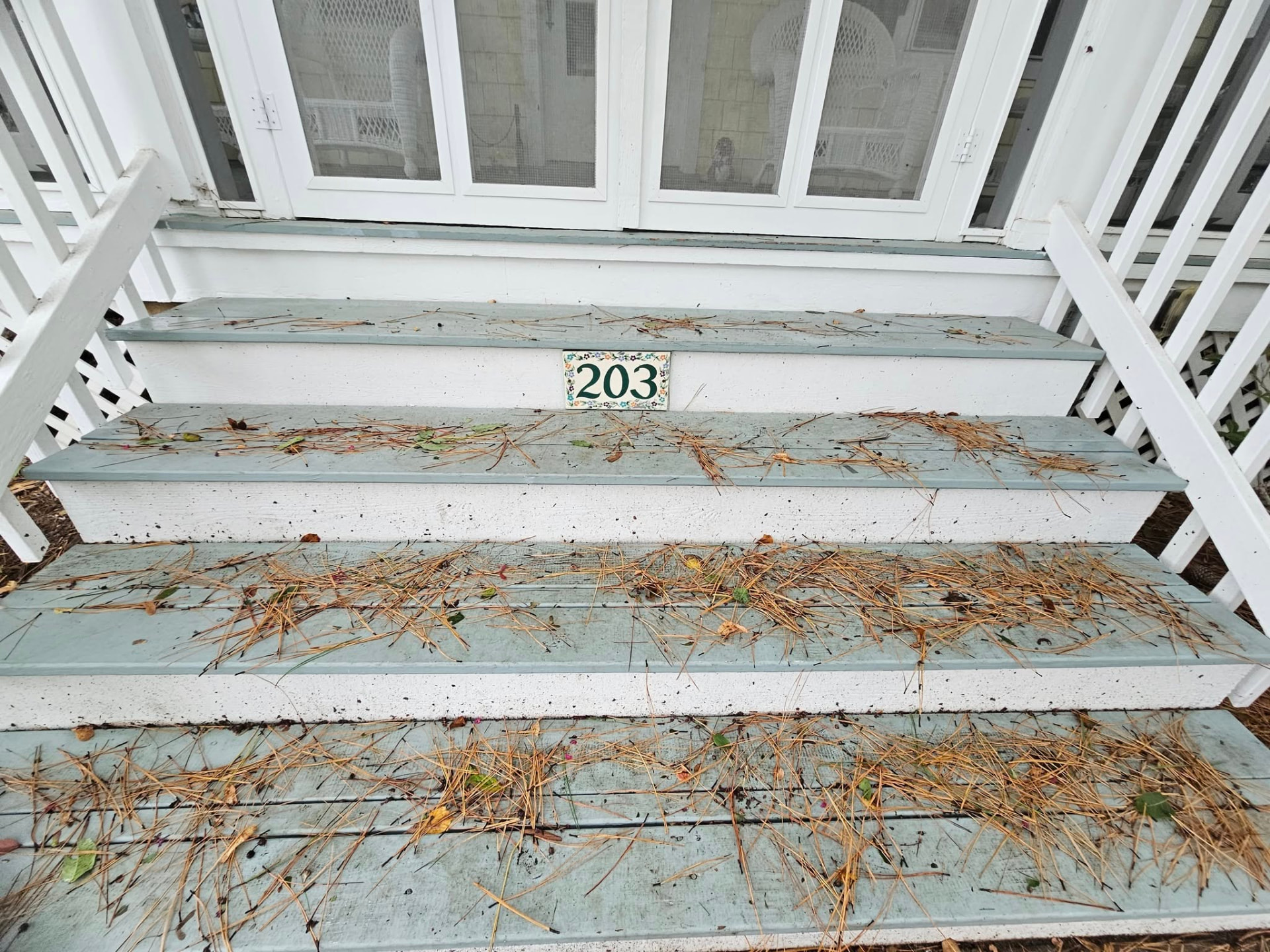 Weathered pale blue porch steps covered in pine needles with worn white risers