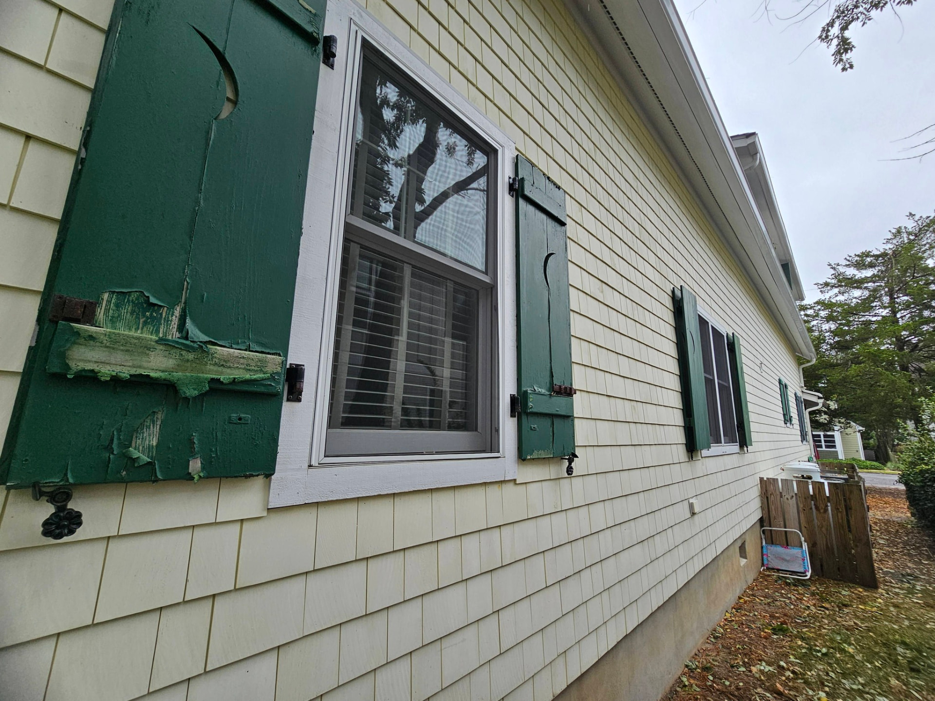 Board-and-batten shutters with green paint peeling to bare wood against sun-faded cream siding