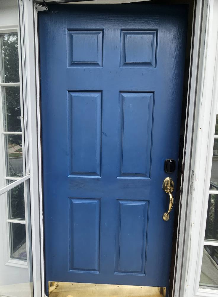 Six-panel front door painted navy blue with brass hardware before repainting