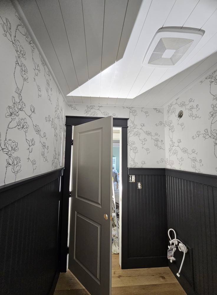 Bathroom with magnolia line-art wallpaper above charcoal beadboard wainscot and a charcoal door