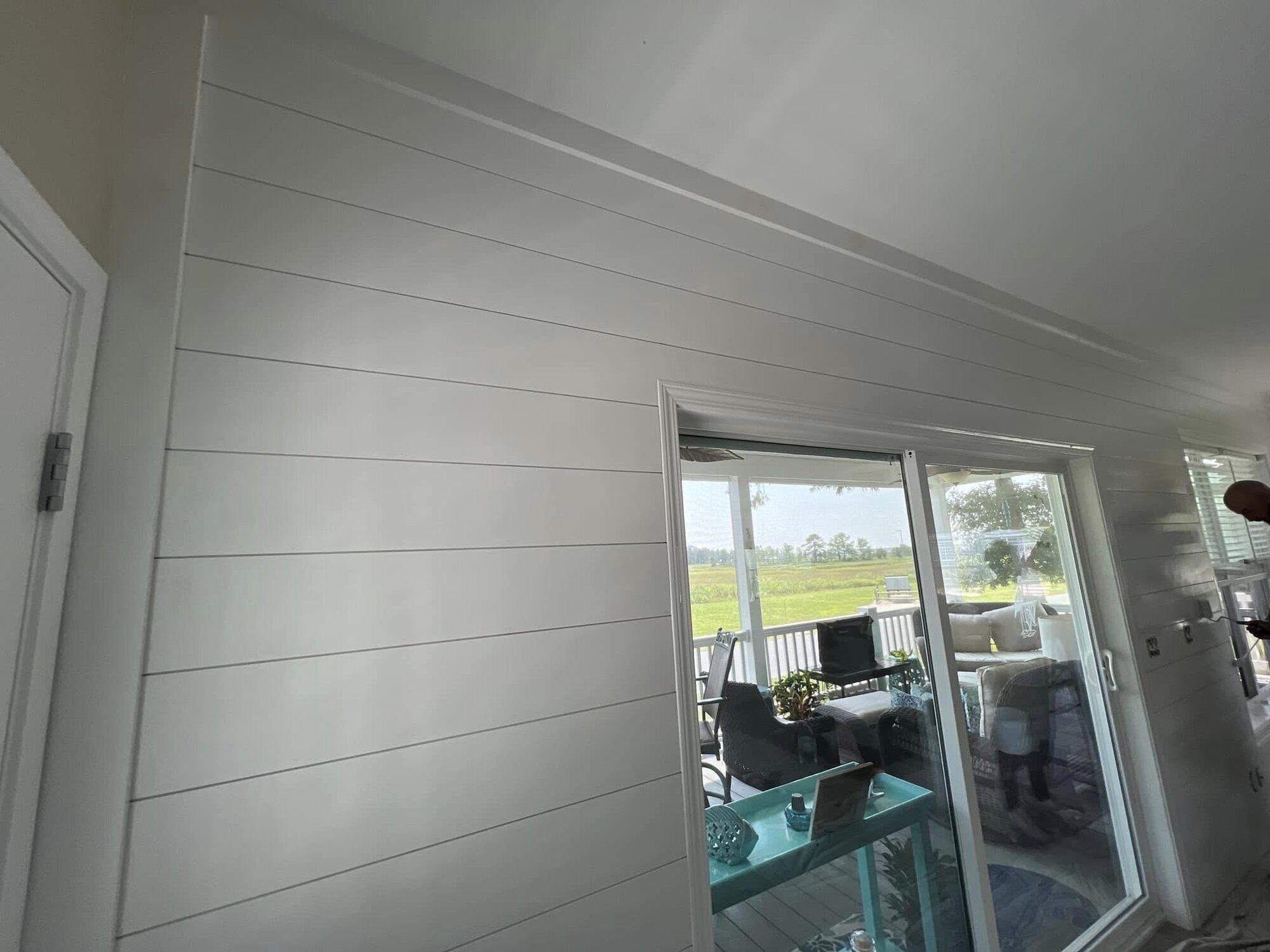 Interior white shiplap wall with clean seams beside a slider to a covered porch