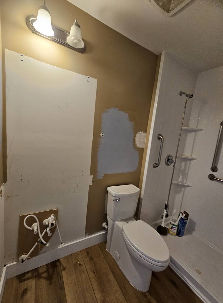 Guest bathroom mid-demo with patched drywall, tan walls, and exposed plumbing before finishing