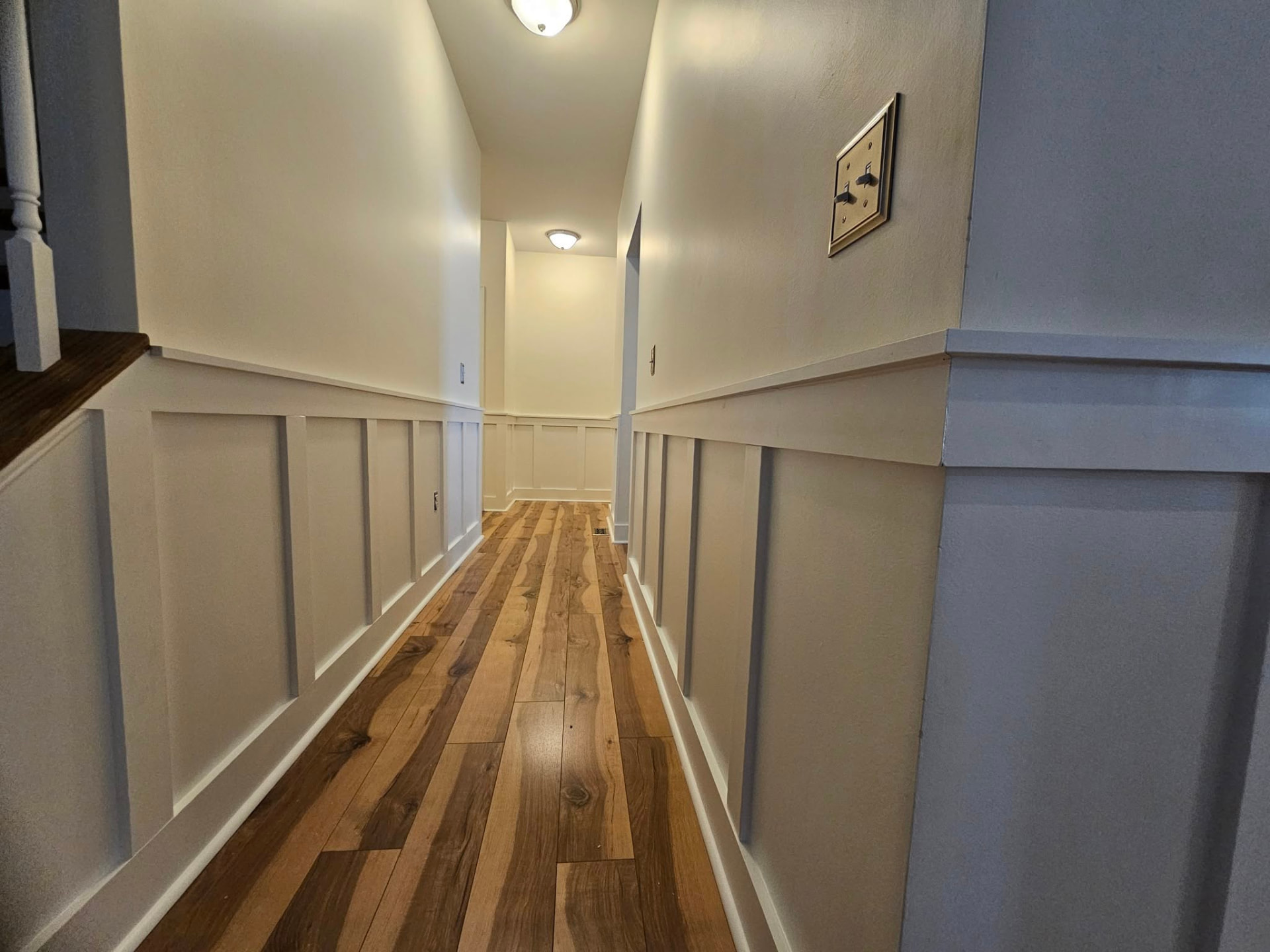 Hallway with full board and batten wainscot painted soft white running the length of the corridor