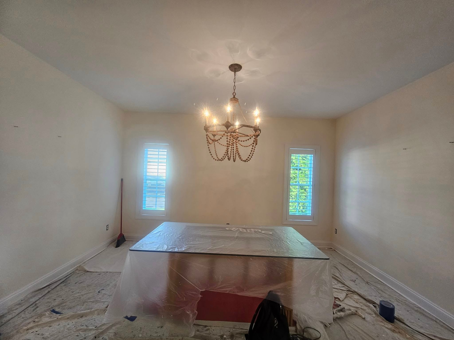 Dining room with plain beige walls, floors covered in drop cloths before painting