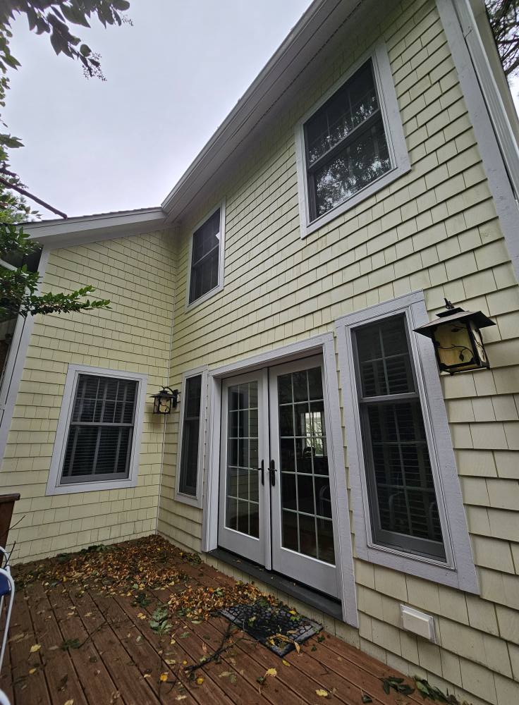 Back elevation with dull, weather-streaked cedar shake siding and grey window trim above a faded deck