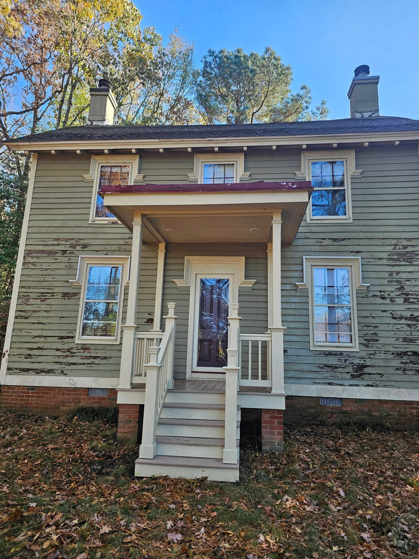Historic two-story farmhouse with heavily peeling green paint and weathered trim before restoration