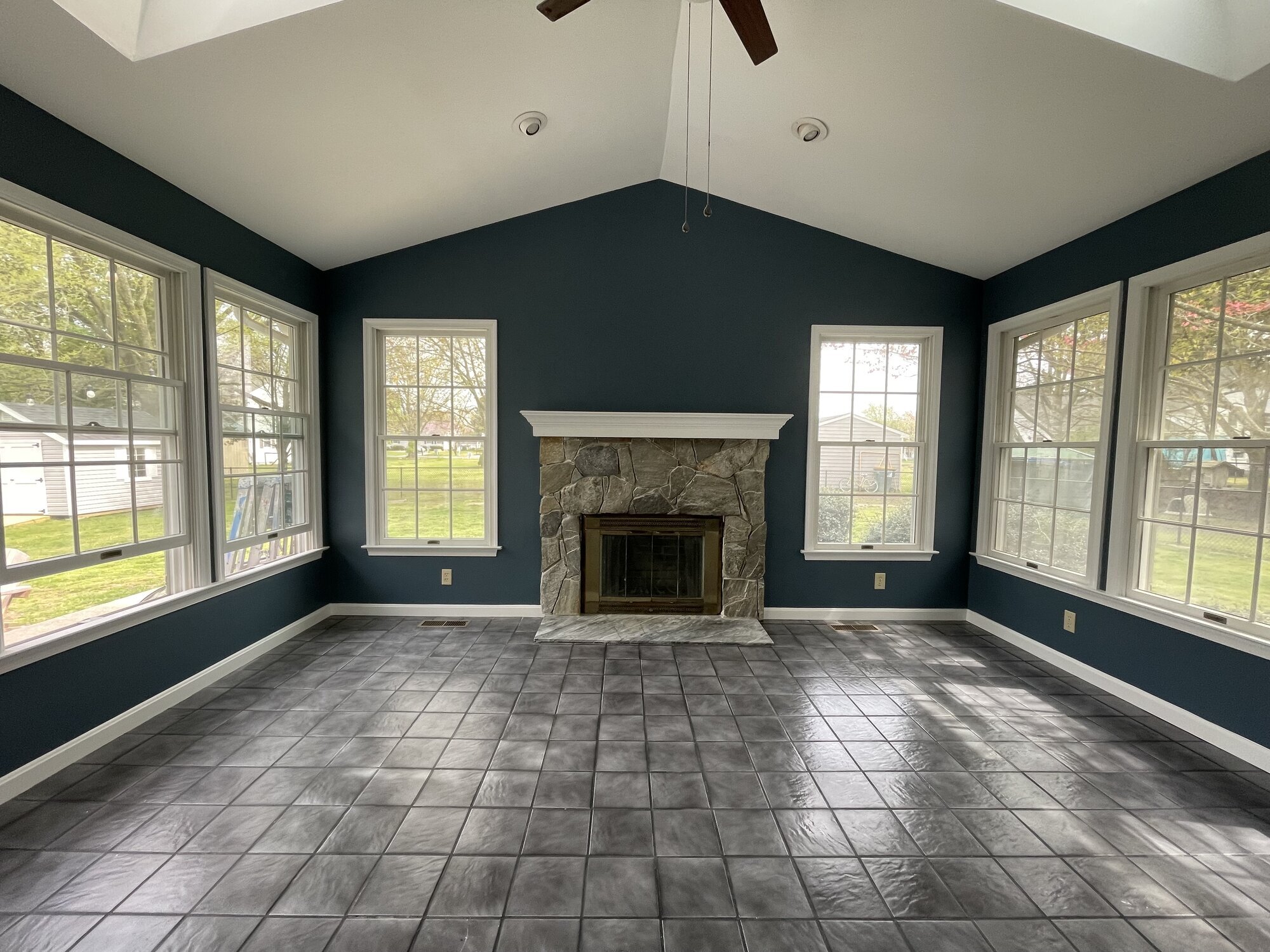 Sunroom painted deep teal-blue with crisp white trim, vaulted white ceiling, and a stone fireplace