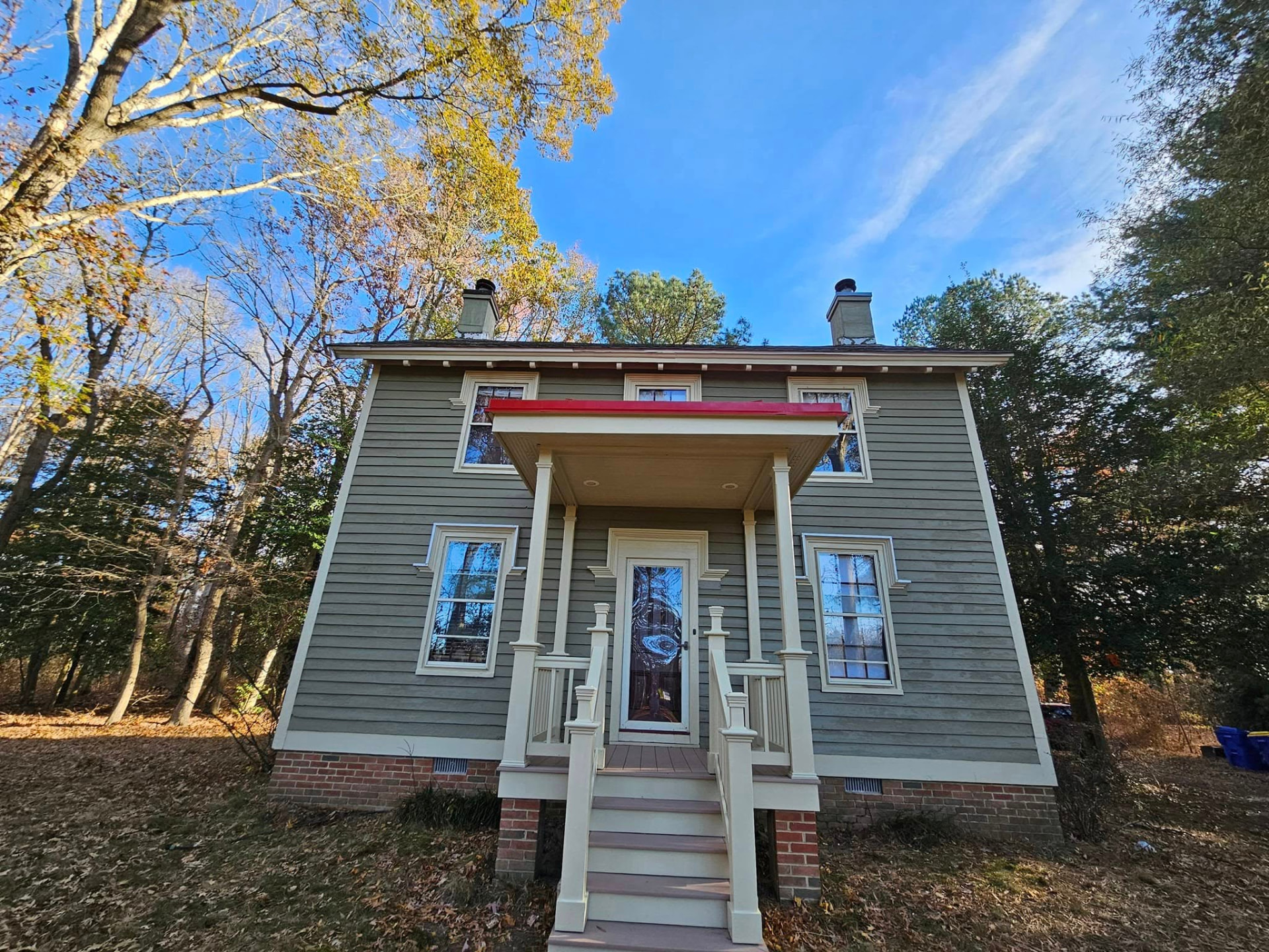 Same farmhouse repainted sage green with cream trim, restored brackets, and a fresh red porch roof
