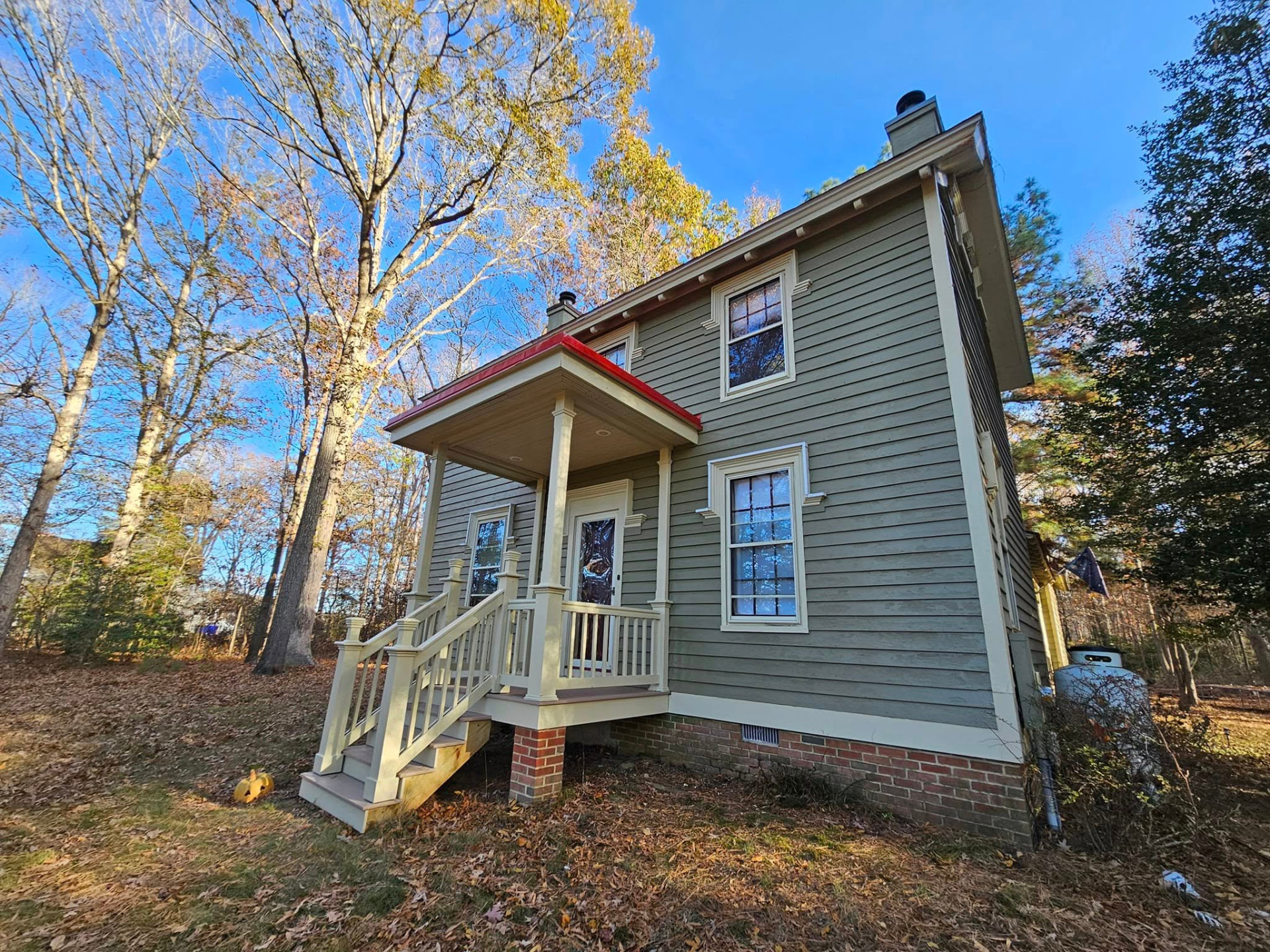 Restored two-story farmhouse painted sage green with cream trim and a red porch roof