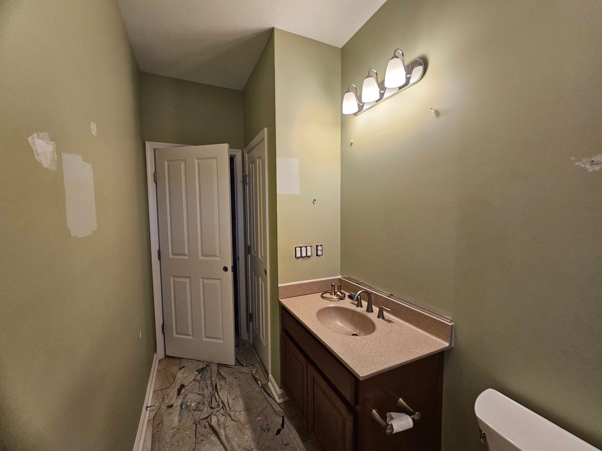 Hall bathroom with dated olive walls, patch marks, and drop cloths on the floor