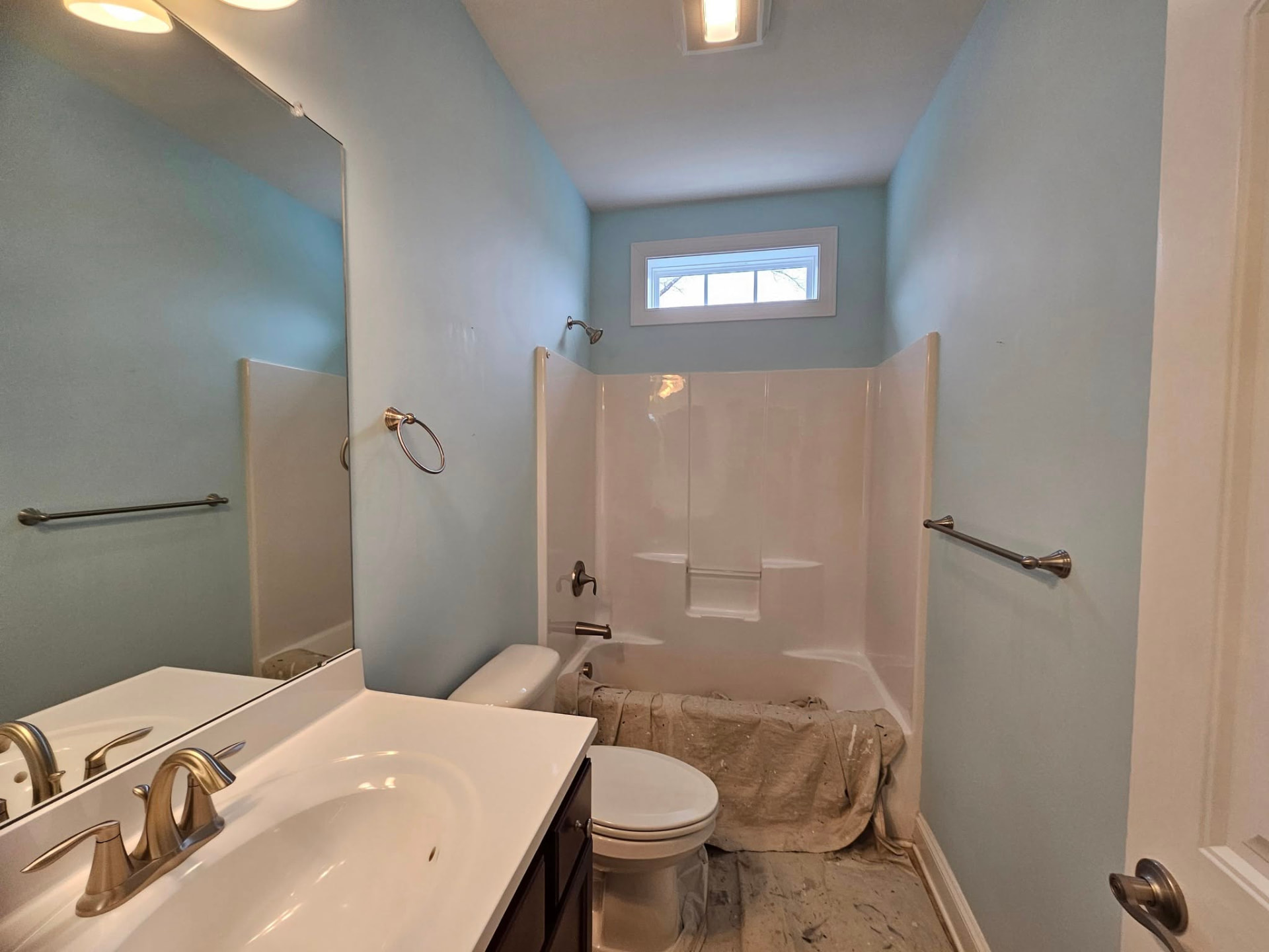 Bathroom with pale blue walls and drop cloths over the tub before repainting