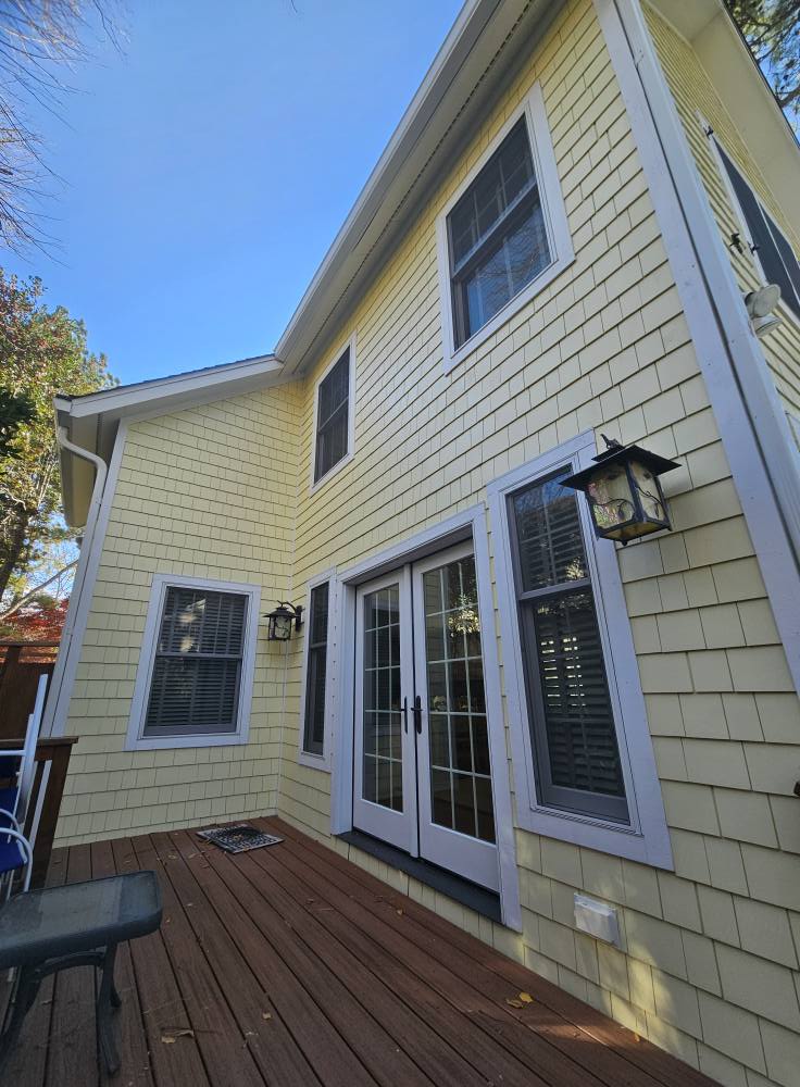 Same elevation with clean butter-yellow shakes, bright white casings, and a freshly stained deck