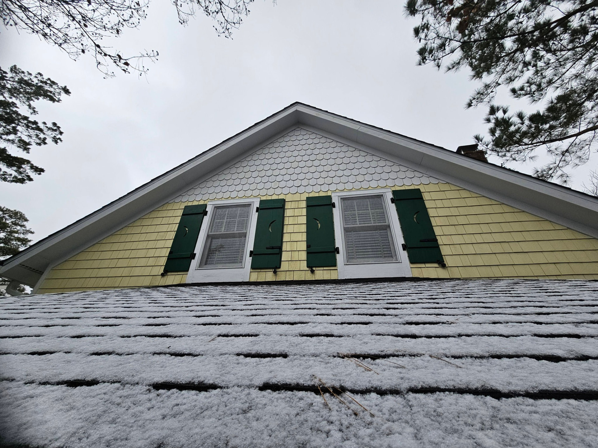 Same gable with deep green shutters, bright white scalloped shingles, and clean butter-yellow siding