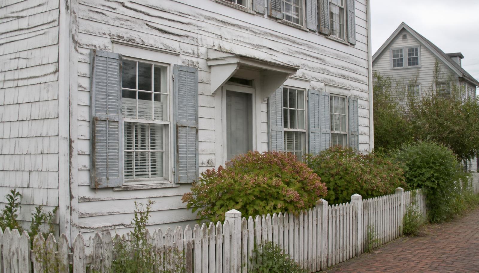 Historic Lewes, Delaware cottage before repainting, showing chalking white clapboard, peeling paint at the sills, and faded grey-blue shutters